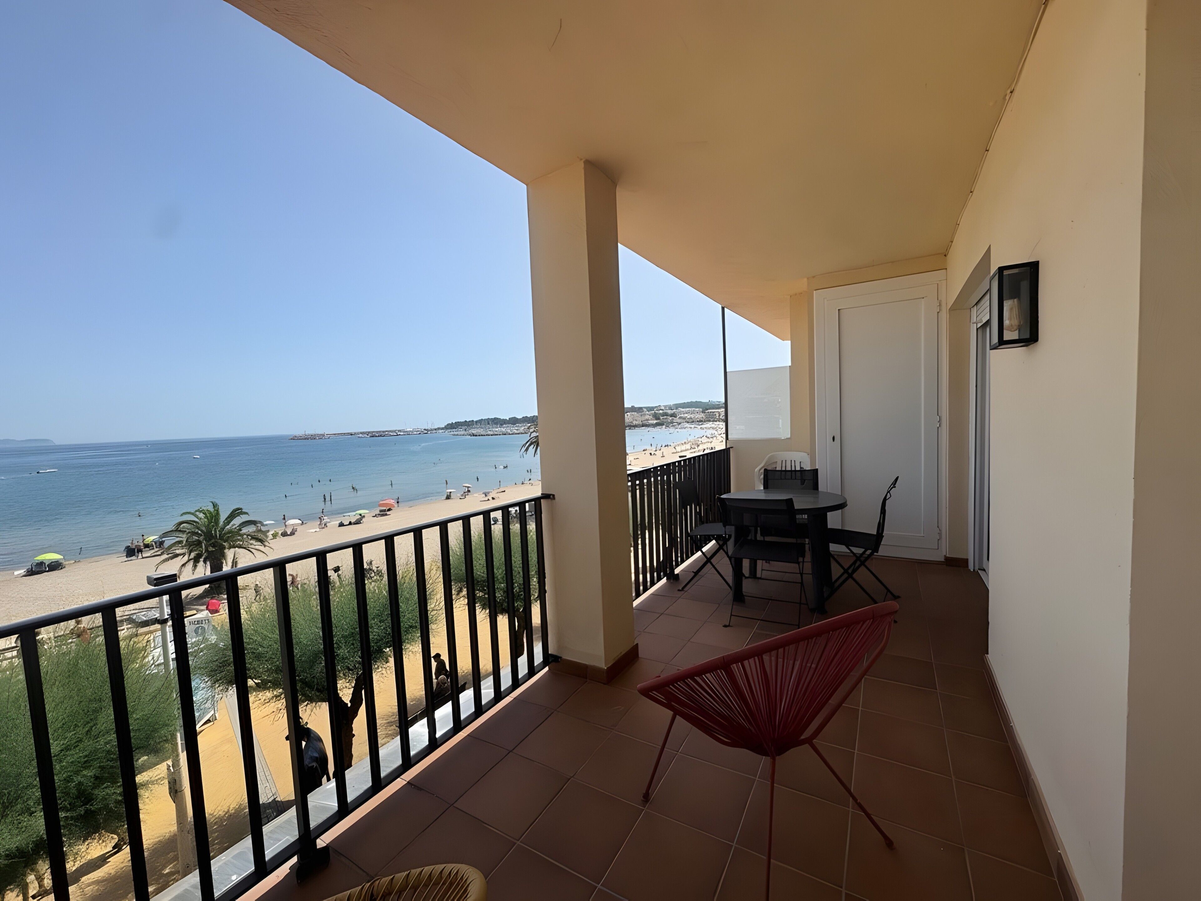 Ein Balkon mit Blick auf den Strand, ein Tisch mit Stühlen und ein roter Sessel.