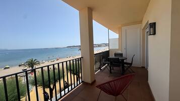 A balcony with a view of the beach, a table with chairs, and a red chair.