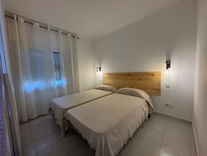 Ein Schlafzimmer mit zwei Betten, einem Holzkopfstück, einem Fenster mit Rollläden und Wandleuchten.