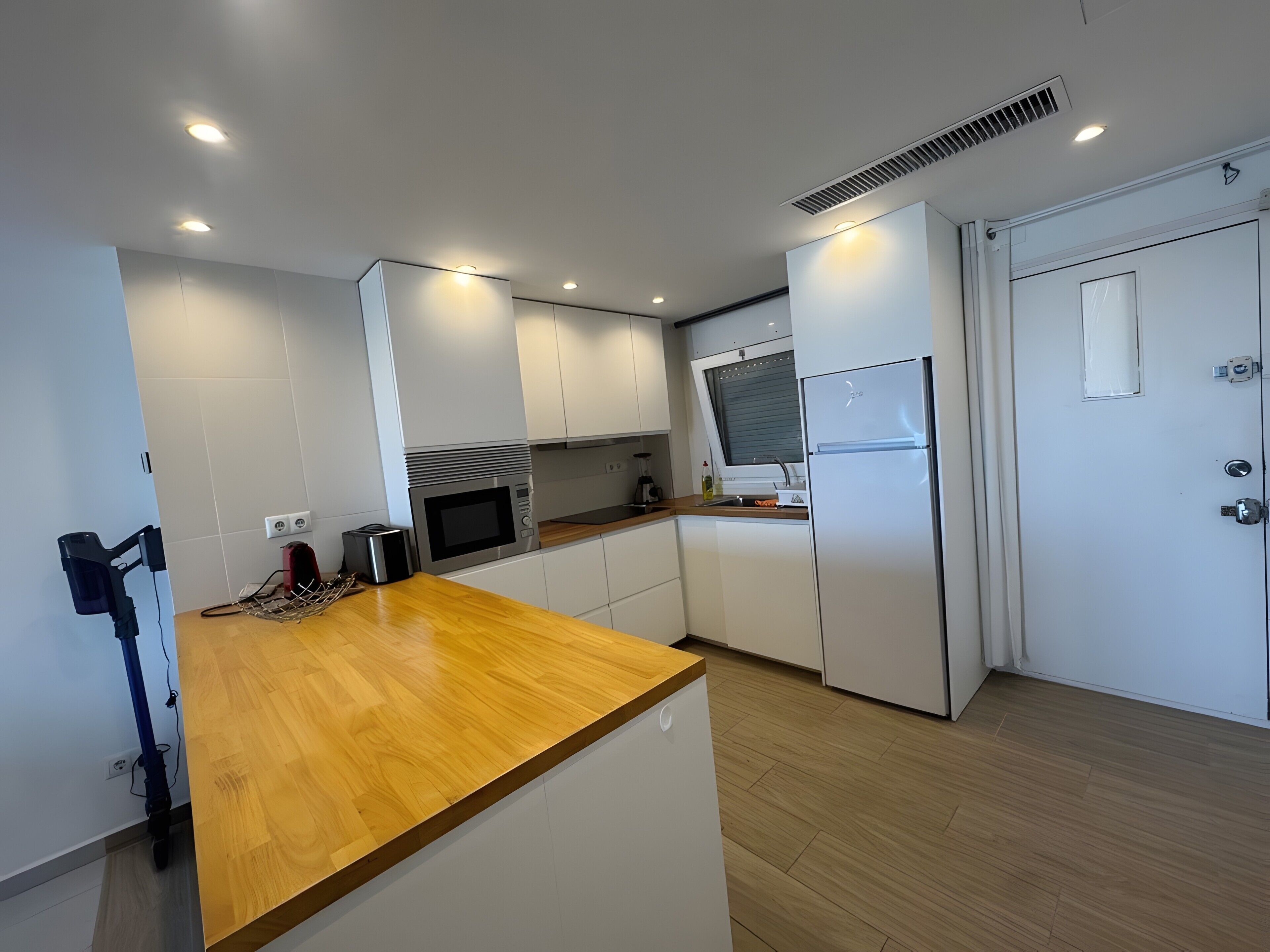 A modern kitchen with white cabinets, a wooden countertop, a built-in microwave, and a refrigerator.