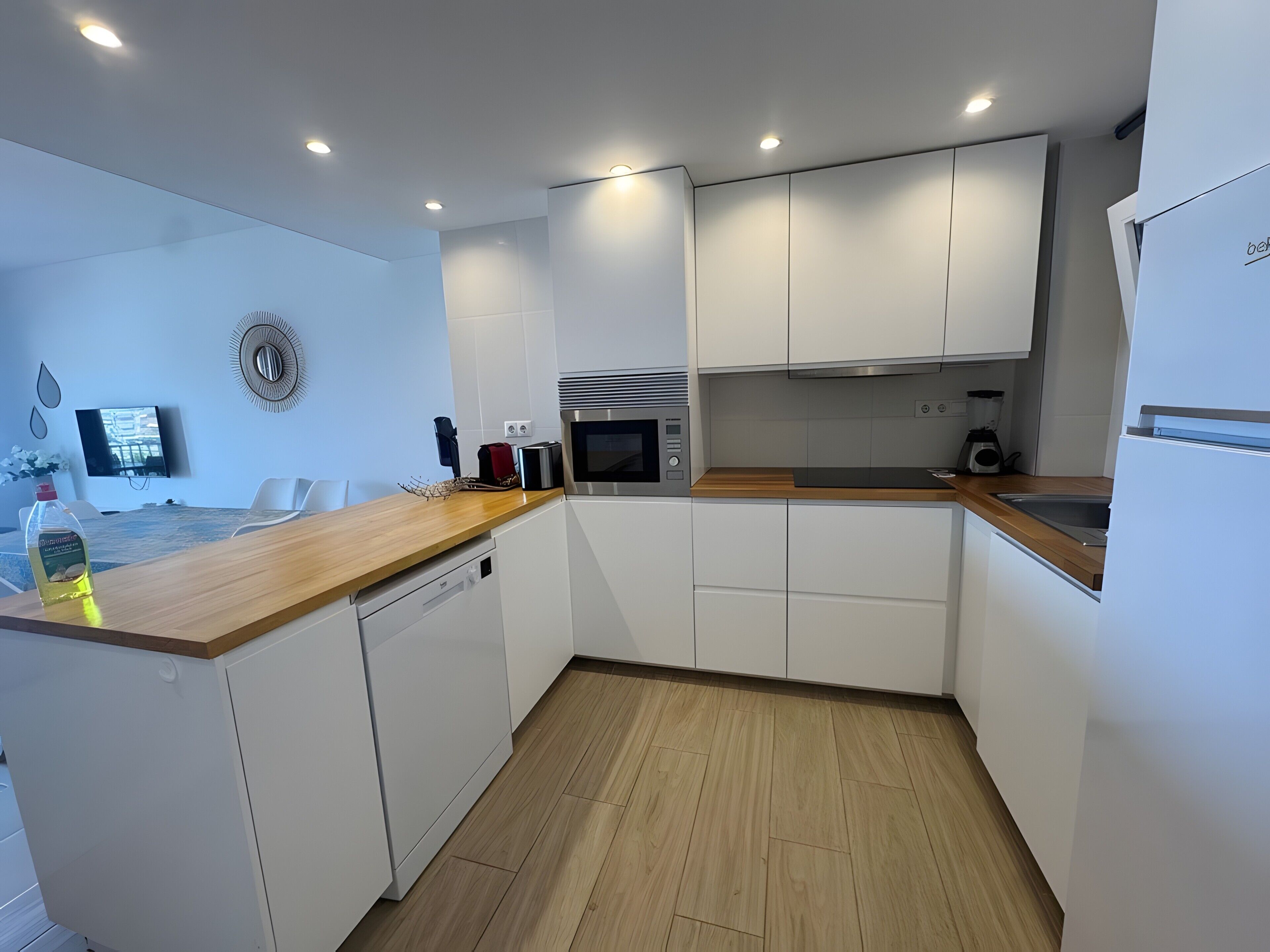 A modern kitchen with white cabinetry, a wooden countertop, a built-in microwave, and a sink.