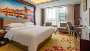 A hotel room with a large bed, two armchairs, a small table, and a view of the cityscape through the window. - Vienna International Hotel (Leshan Shizhong District Store) (Leshan)