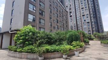 A high-rise residential building with a landscaped courtyard featuring potted plants and a concrete pathway.