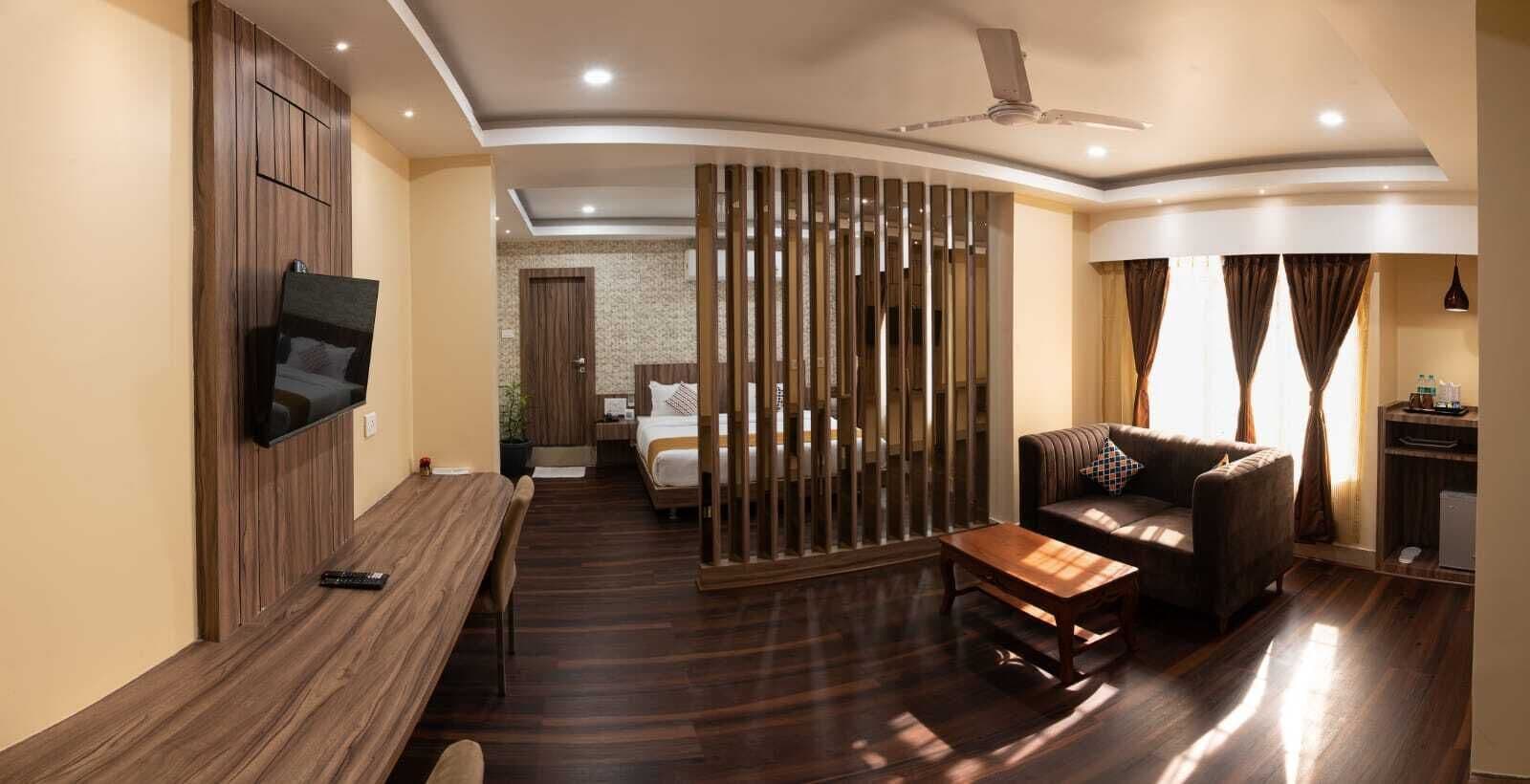 Habitación de hotel moderna con una televisión de pantalla plana montada en la pared, un sofá, una mesa de centro y una cama con cabecera de madera.