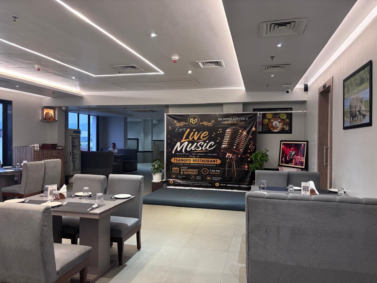 A modern restaurant interior with a live music stage, seating arrangements, and a view of the cityscape.