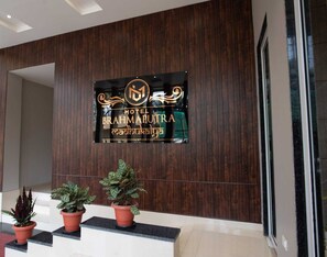 Un letrero de hotel con el nombre 'Hotel Brahmaputra' y un logotipo. Hay tres plantas en macetas sobre un alféizar frente al letrero.