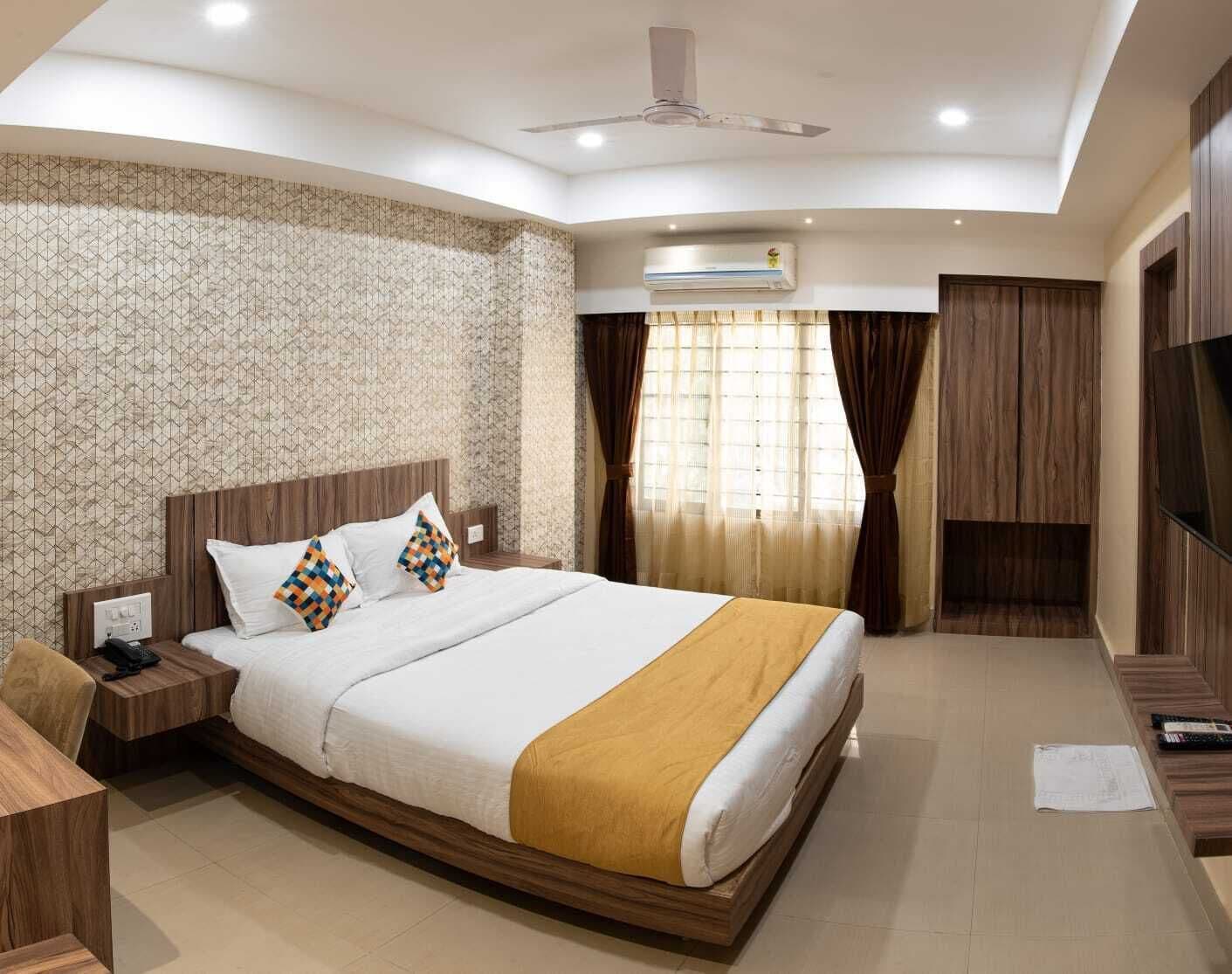 A hotel room with a bed, bedside table, lamp, TV, and a ceiling fan.