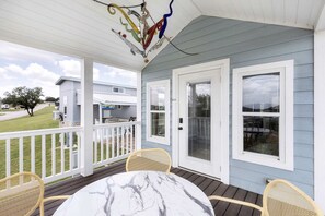 En overdækket veranda med et bord og stole, udsigt til et hus og en dekorativ hængende lampe.