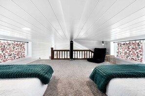 A room with two beds, a black chair, a wooden railing, and a window with patterned curtains. - Peaceful Tiny Home Retreat with Pool and Resort Access Near Fredericksburg, TX (Fredericksburg)