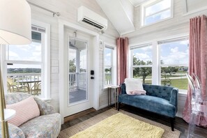 A room with a blue sofa, a patterned armchair, a small table, and a view of a green landscape through large windows. - Peaceful Tiny Home Retreat with Pool and Resort Access Near Fredericksburg, TX (Fredericksburg)