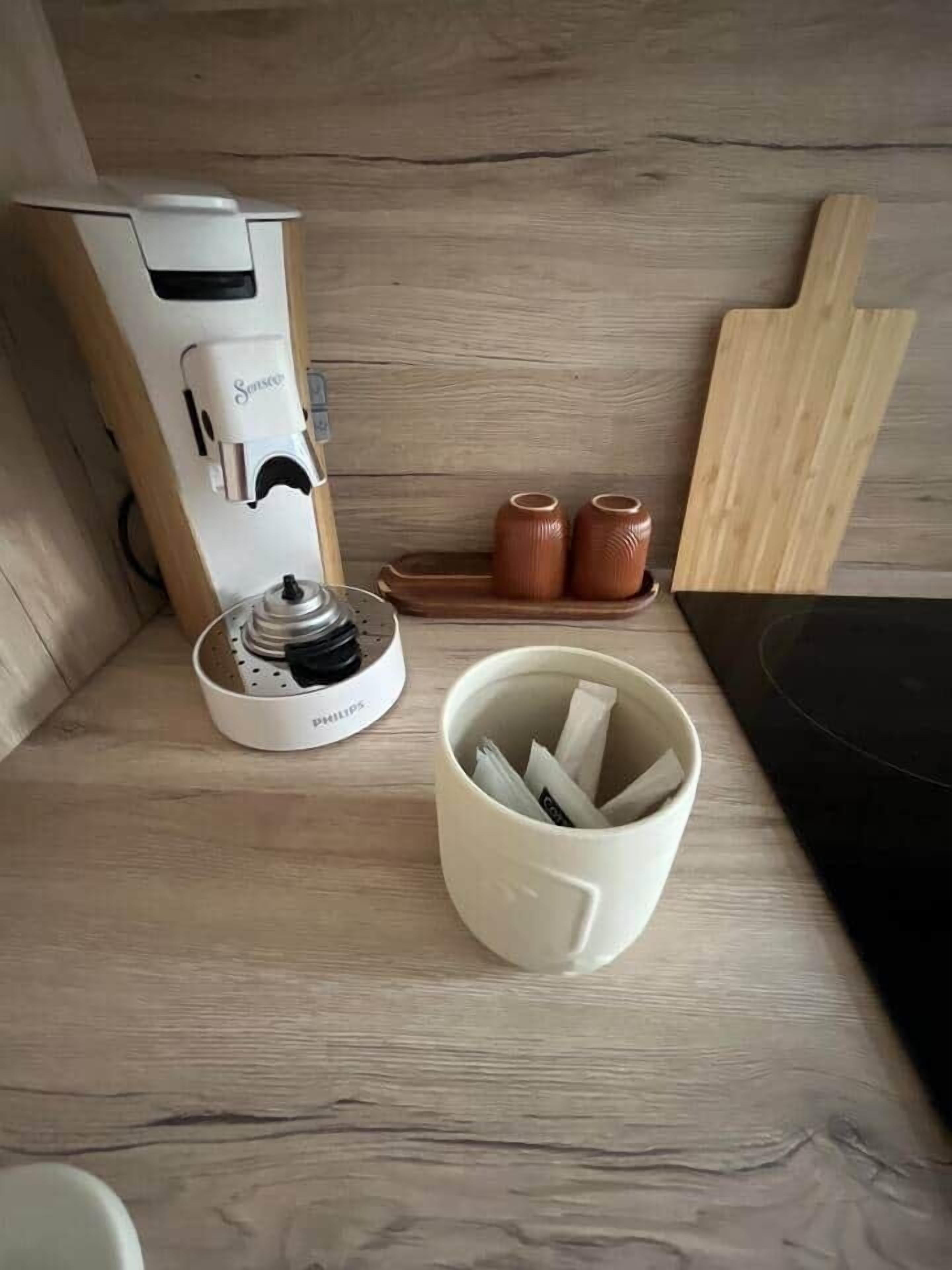 Ein Holztisch mit einer weißen Philips-Kaffeemaschine, einer Keramiktasse und einem Holzschneidebrett.