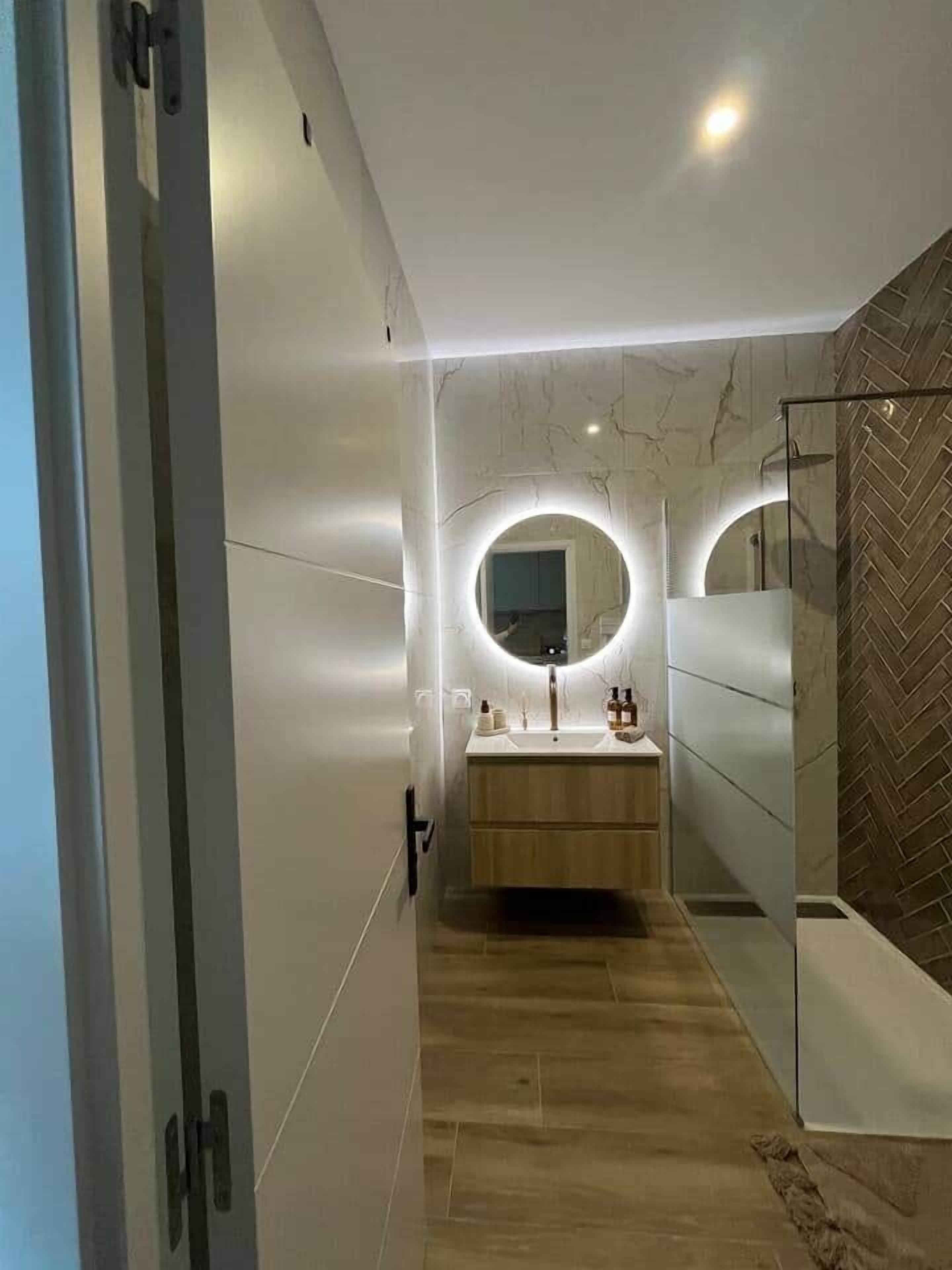 Ein modernes Badezimmer mit Waschtisch, Spiegel und Beleuchtung.