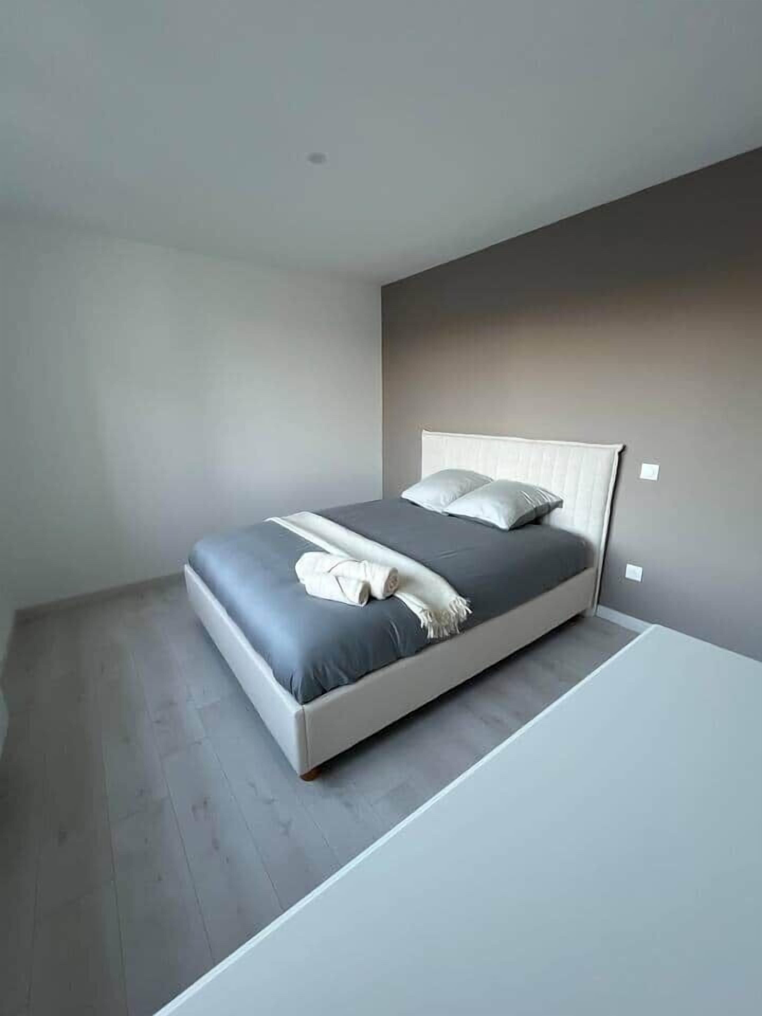 A modern bedroom with a bed, a bedside table, and a wall-mounted light fixture.