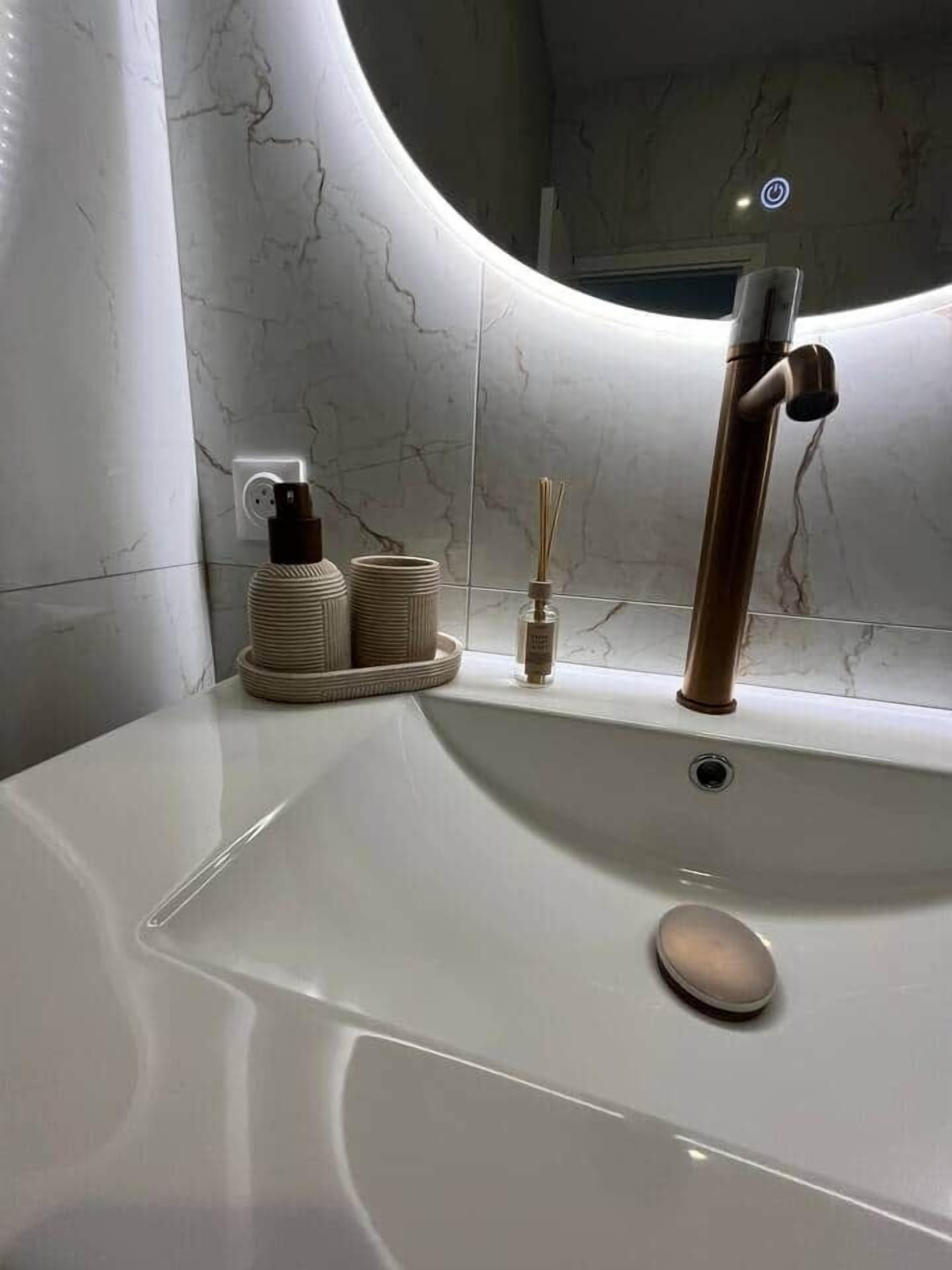 Un bany amb un lavabo blanc, un aixeta modern i una paret de marbre.