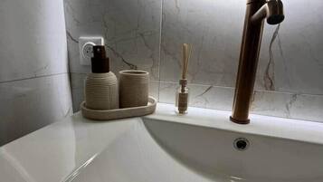 Un bany amb un lavabo blanc, un aixeta modern i una paret de marbre.