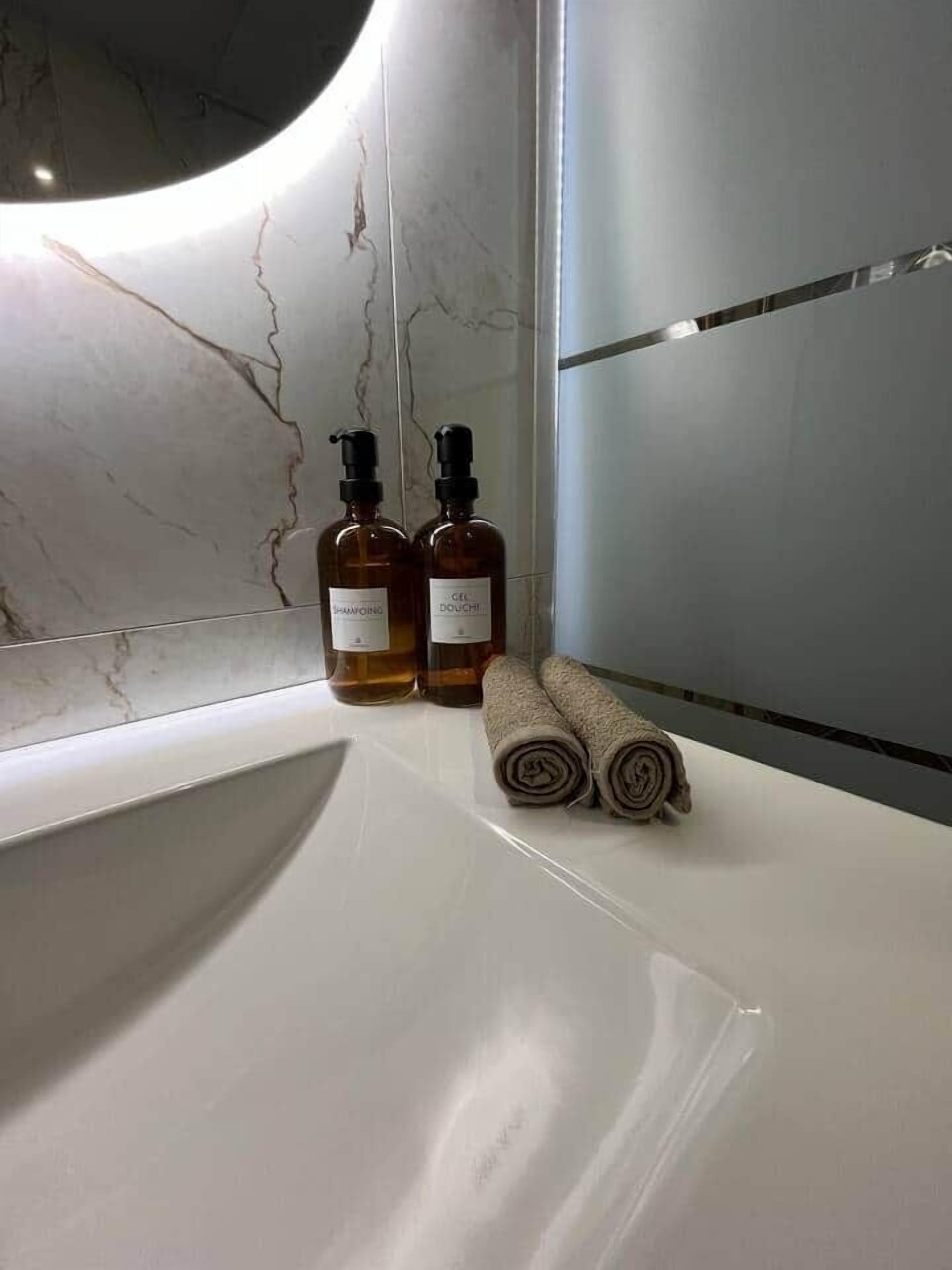 Un baño con un lavabo blanco, dos botellas de champú y acondicionador, y toallas dobladas.
