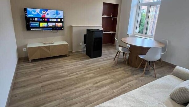 En stue med et fladskærms-tv, en sofa, et spisebord med stole og et vindue.