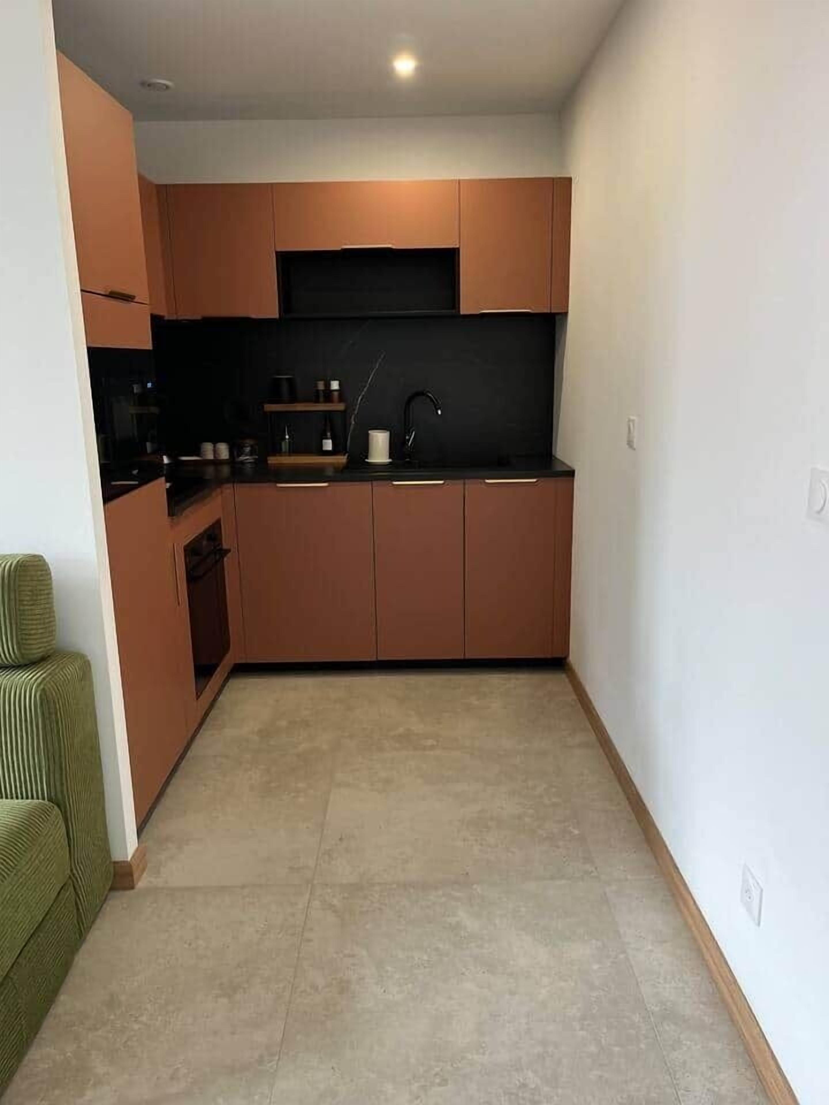 Een kleine keuken met moderne kastjes, een zwart aanrecht en een groene stoel.