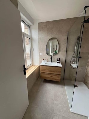 A modern bathroom with a large mirror, wooden vanity, and a glass shower enclosure. - Bayt al Nour | Designer & Cozy Apartment (Givet)