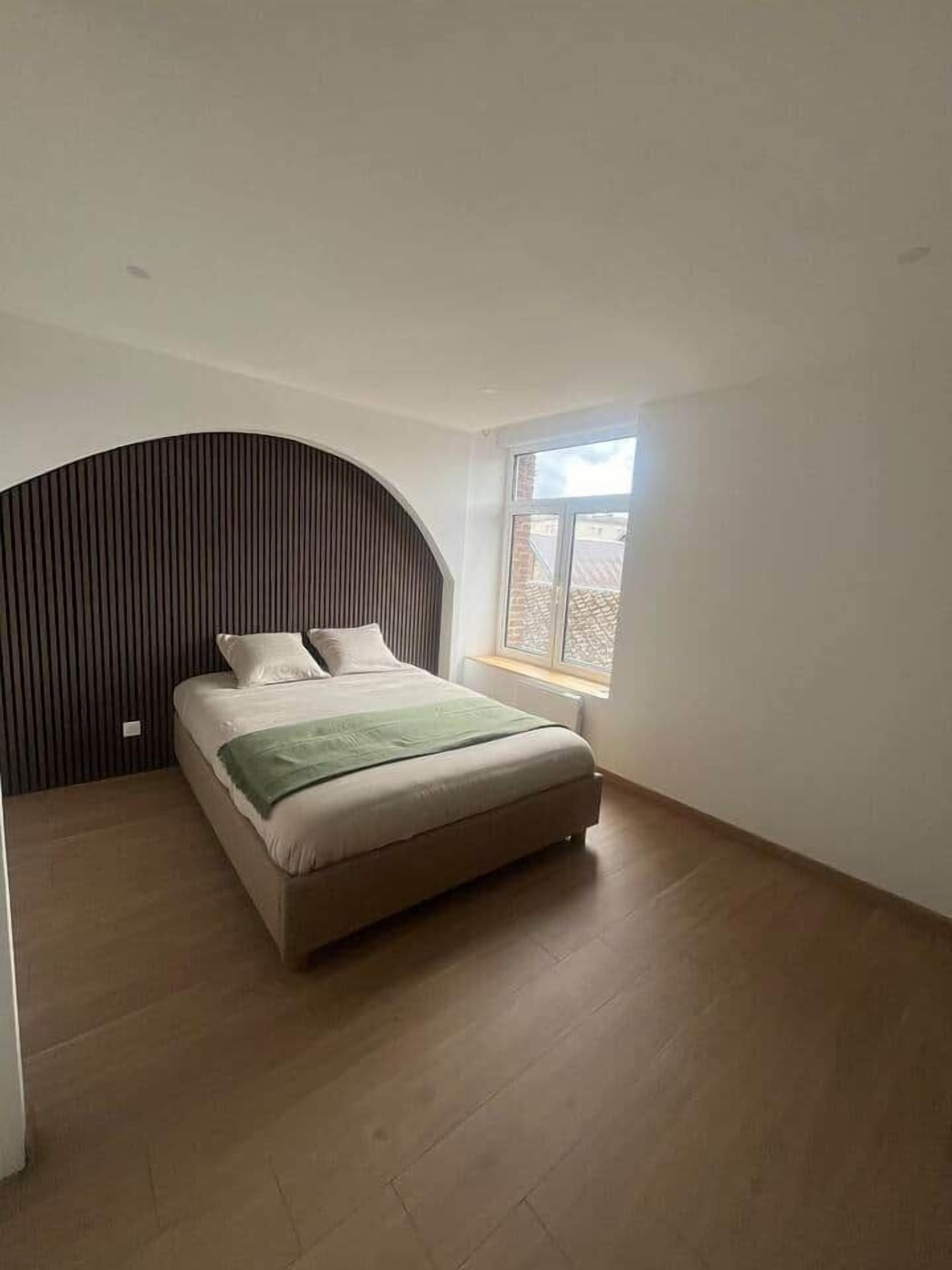 Een slaapkamer met een bed, een raam en een gebogen muur.