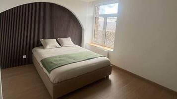 Een slaapkamer met een bed, een raam en een gebogen muur.