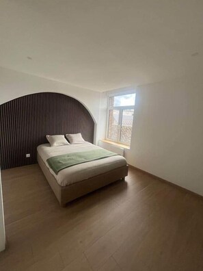A bedroom with a bed, a window, and a curved wall. - Bayt al Nour | Designer & Cozy Apartment (Givet)