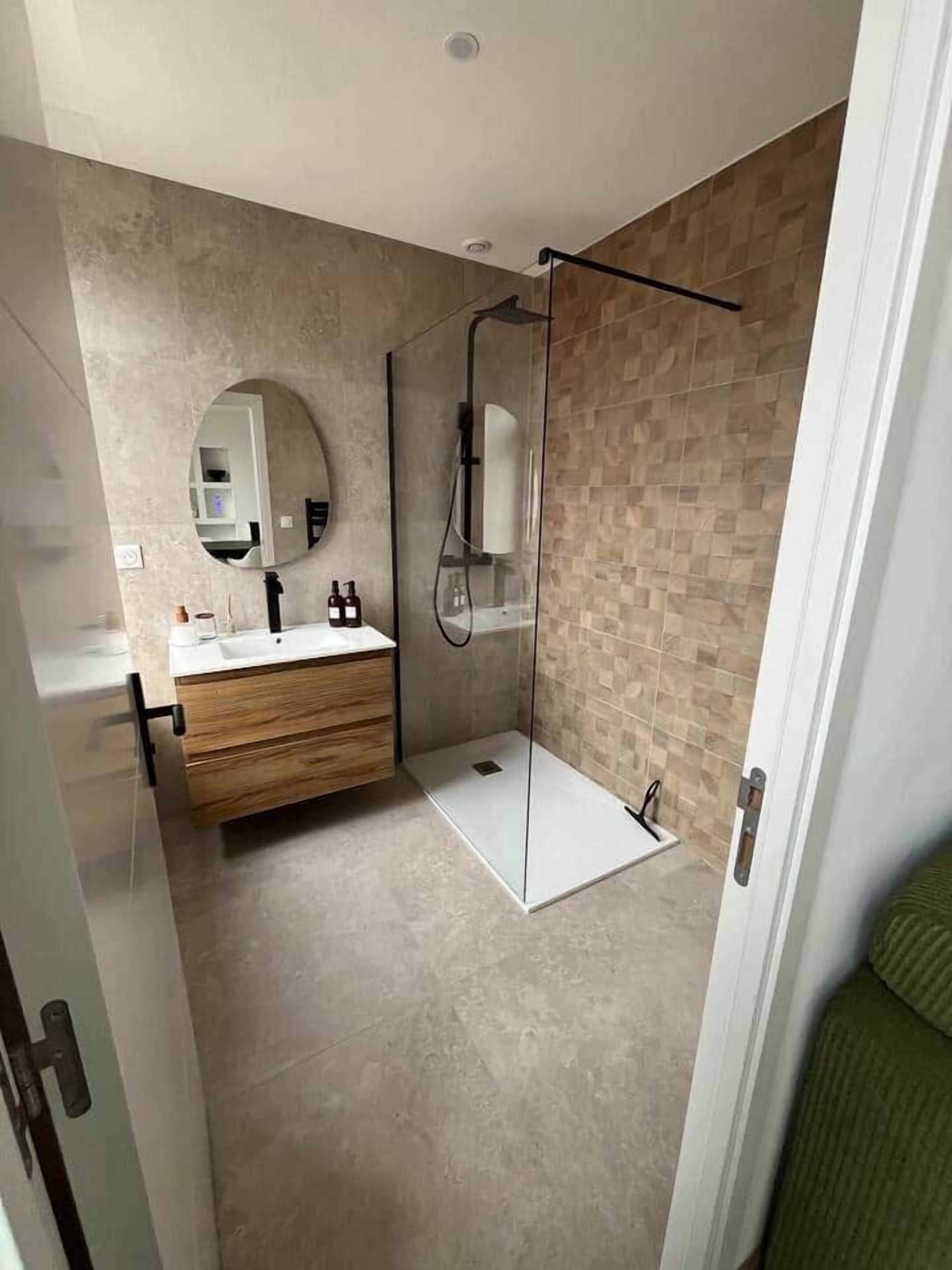 Een moderne badkamer met een glazen douchecabine, een houten wastafelmeubel en een grote spiegel.