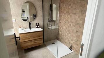 Een moderne badkamer met een glazen douchecabine, een houten wastafelmeubel en een grote spiegel.