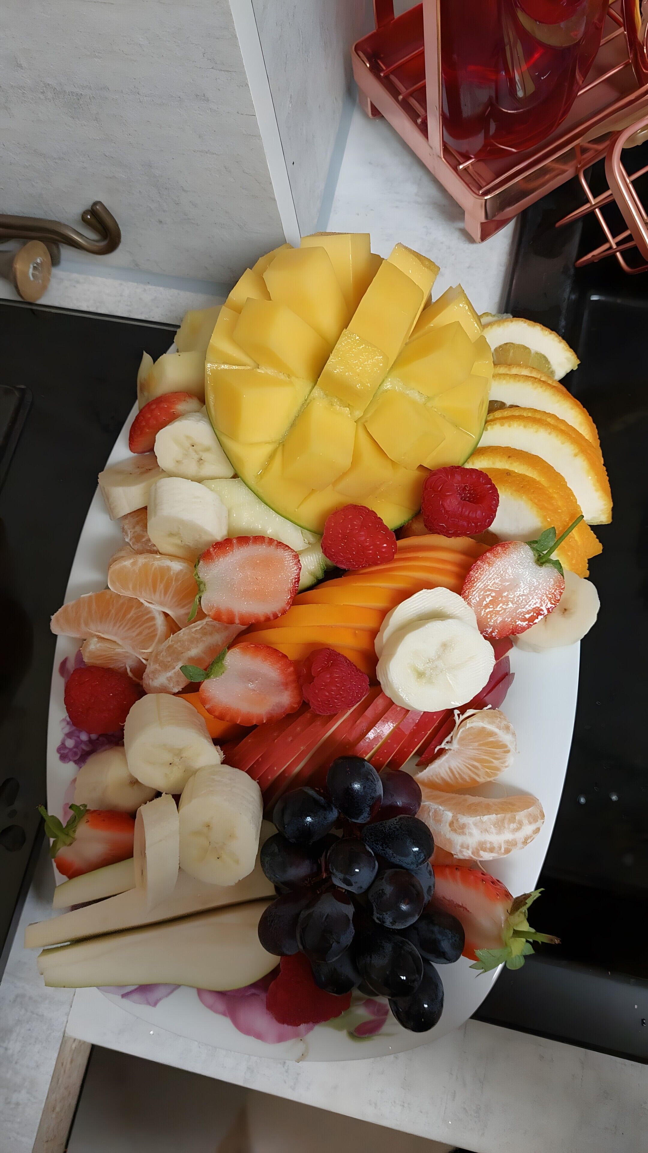 A fruit platter with various fruits including mango, strawberries, bananas, grapes, and oranges.