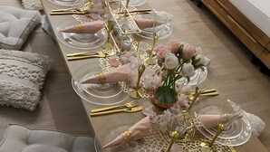 A long dining table with clear glassware, gold cutlery, and pink flowers.
