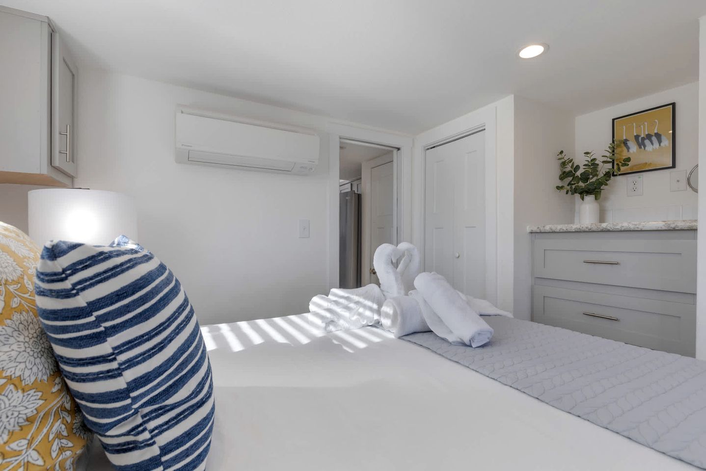 A hotel room with a bed, a bedside lamp, a towel, a plant, and a painting on the wall.