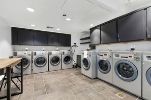 A laundry facility with multiple washing machines, a table, and cabinets. - Modern and Inviting Tiny Home Retreat with Resort-Style Pool and Amenities Near Fredericksburg, TX (Fredericksburg)
