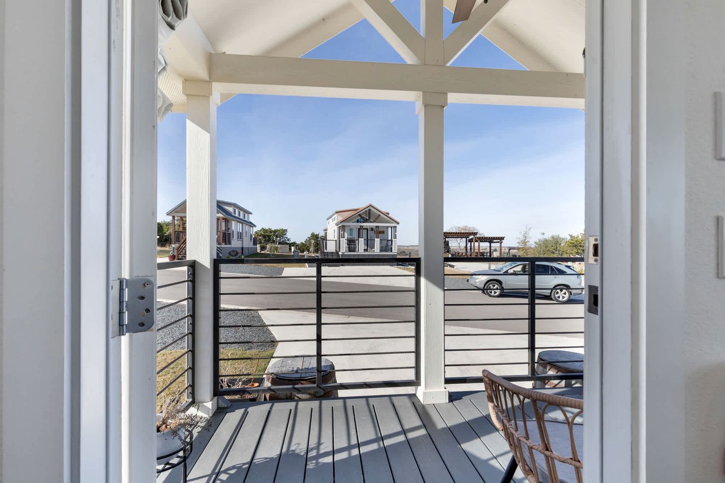 A covered outdoor area with a view of a residential street, a gated entrance, and a wooden deck.