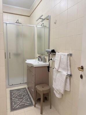 Ein Badezimmer mit Dusche, Waschbecken, Spiegel, Handtuchhalter und einem kleinen Hocker.