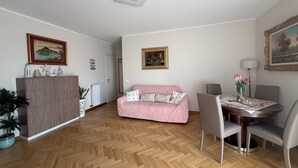 Una sala de estar con piso de espiga, un sofá rosa, una mesa de comedor con sillas y un radiador.
