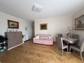 A living room with a herringbone floor, a pink sofa, a dining table with chairs, and a radiator. - Fede's House (Sestri Levante)