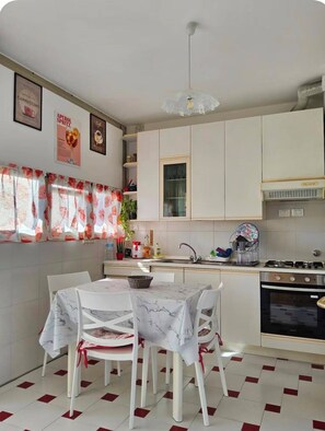 A modern kitchen with white cabinets, a gas stove, and a dining area with a table and chairs. - Fede's House (Sestri Levante)