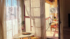 Una habitación con piso de madera, una mesita y una ventana con cortinas traslúcidas.