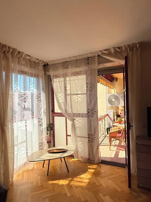 A room with a wooden floor, a small table, and a window with sheer curtains. - Fede's House (Sestri Levante)