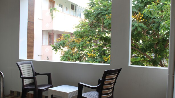 A room with two chairs and a small table, a window with a view of a building and trees. - Swamy Ramana Residency (Tiruvannamalai)
