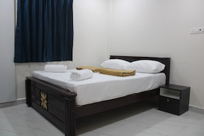 A single bed with white linens, a wooden headboard, and a nightstand. - Swamy Ramana Residency (Tiruvannamalai)