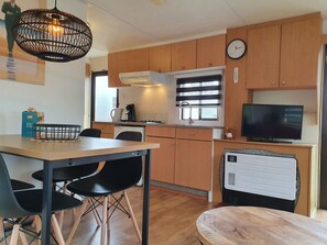 Eine kompakte Küche mit Holzschränken, ein Essbereich mit Stühlen, ein Fernseher und eine eingebaute Heizung.