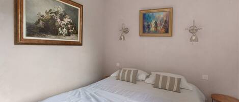Une chambre à coucher avec un grand lit, deux lampes fixées au mur et deux œuvres d’art encadrées.