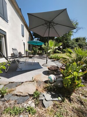 A patio with outdoor furniture, a large umbrella, and a garden with various plants.