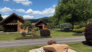 A log cabin with a porch, surrounded by well-maintained lawns and a large rock feature.