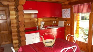 A wooden cabin interior with a red kitchen, white dining table, and chairs.
