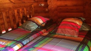 A cabin with a wooden interior, two beds with colorful bedding, and a sloped ceiling.