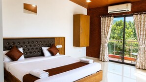 A hotel room with a large bed, a wooden headboard, a built-in air conditioning unit, and a view of greenery through the window. - Hotel green crystal (Mahabaleshwar)