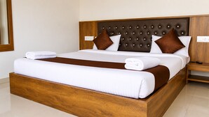 A hotel room with a wooden bed frame, white bedding, and a brown headboard. - Hotel green crystal (Mahabaleshwar)