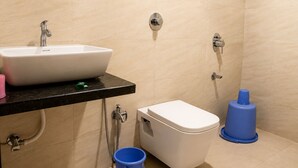 A bathroom with a white sink, toilet, and bidet, with a black countertop and beige tiled walls. - Hotel green crystal (Mahabaleshwar)